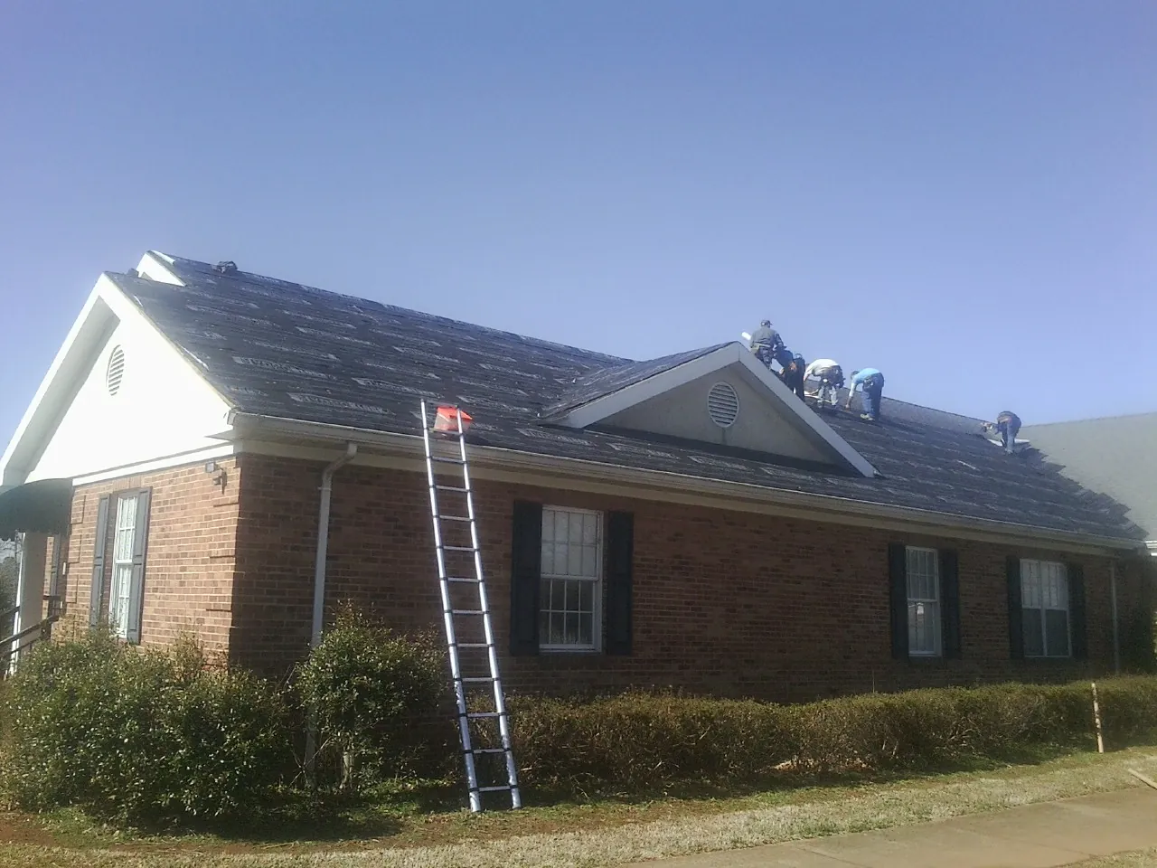 Crew tearing shingles off a brick ranch roof with a ladder set — Metal Roof Repair work by our crew in Trivoli