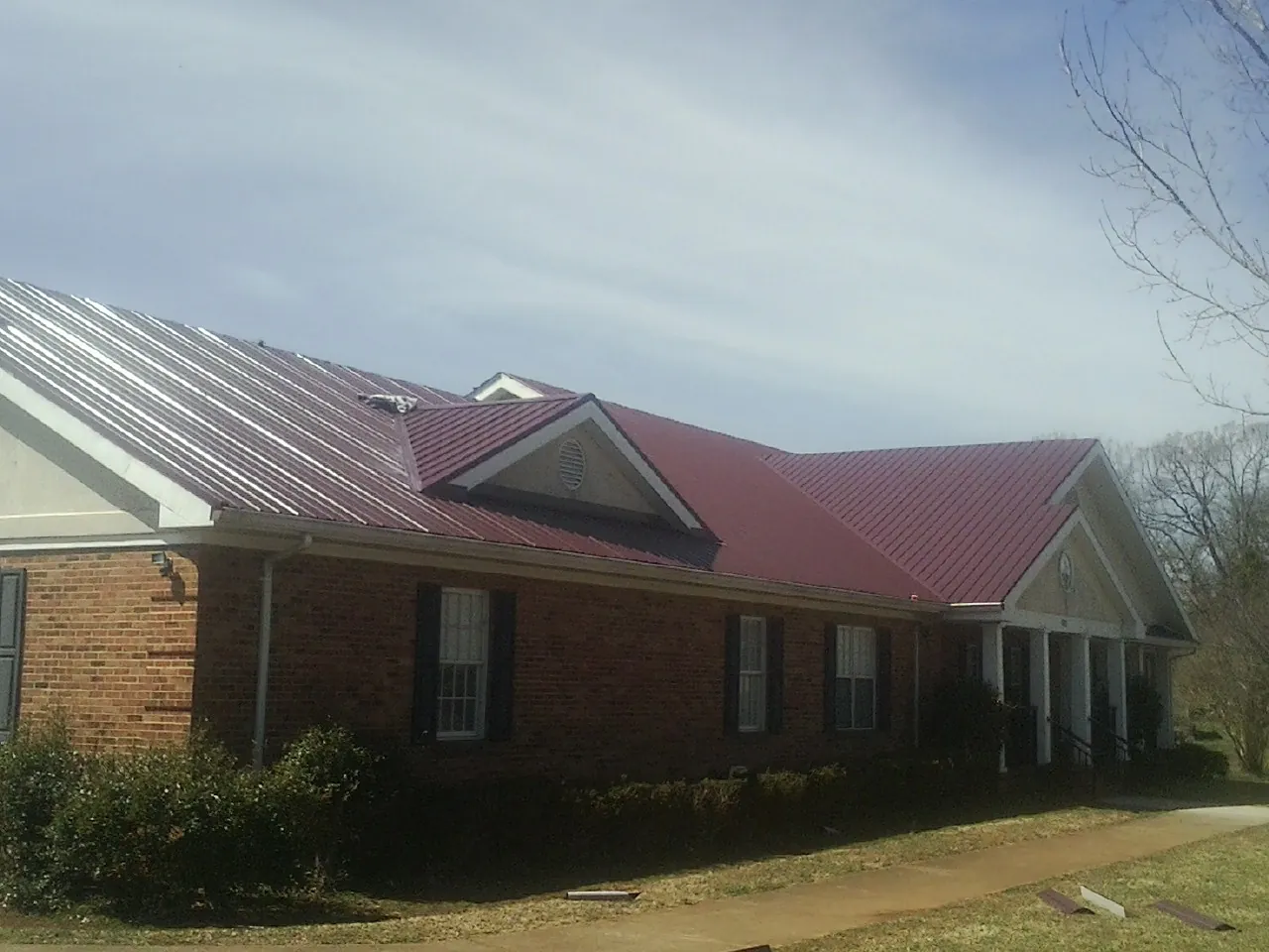 Red metal roof with gabled entries on a long brick building, from a Hail Damage Roof Repair job in Trivoli