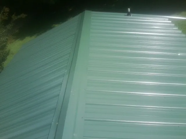 New green metal panels meeting at the ridge of a roof — Flat Roof Repair work by our crew in Trivoli