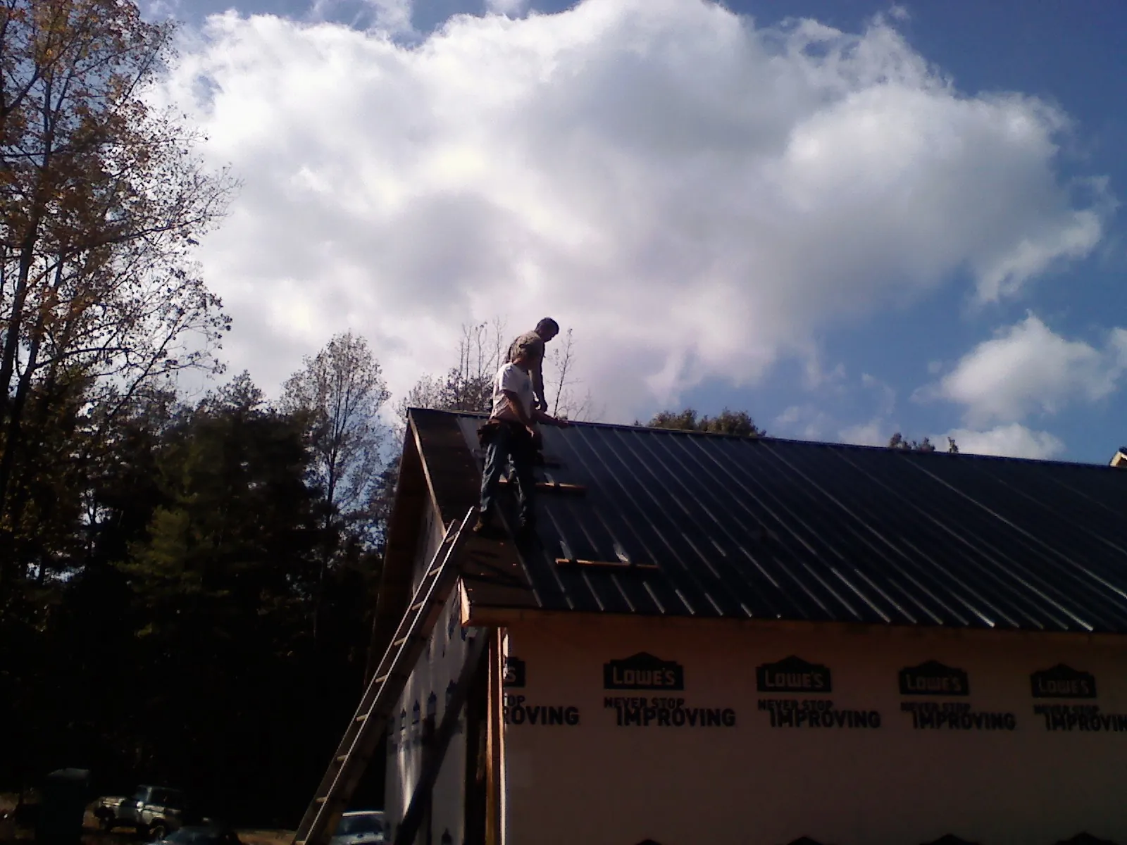 Roofer fastening dark metal panels high against a cloudy sky, from a Roof Inspection job in Trivoli