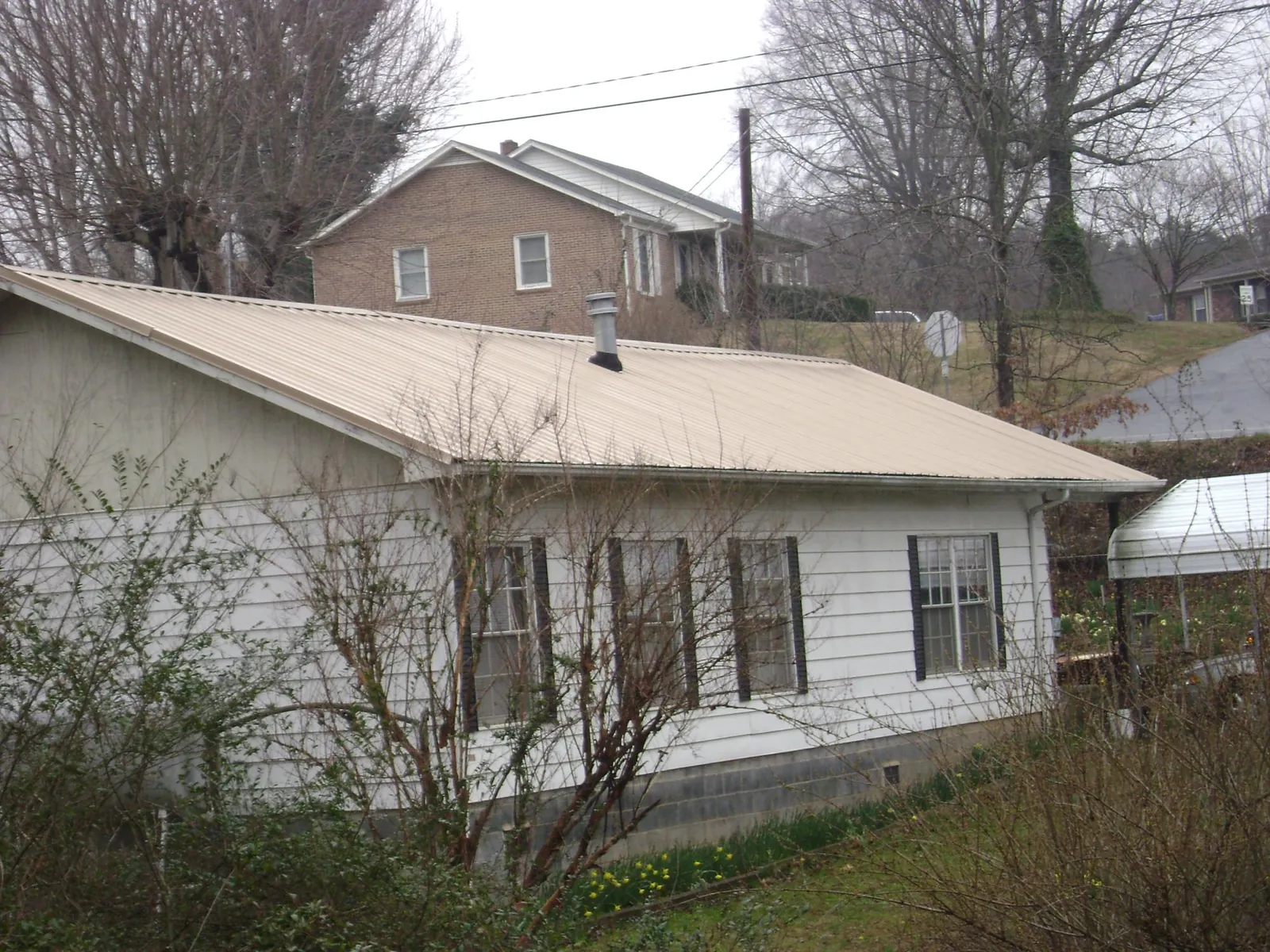 Tan metal roof on a white sided house set into a hillside — Commercial Roofing by Roofing Brothers in Trivoli