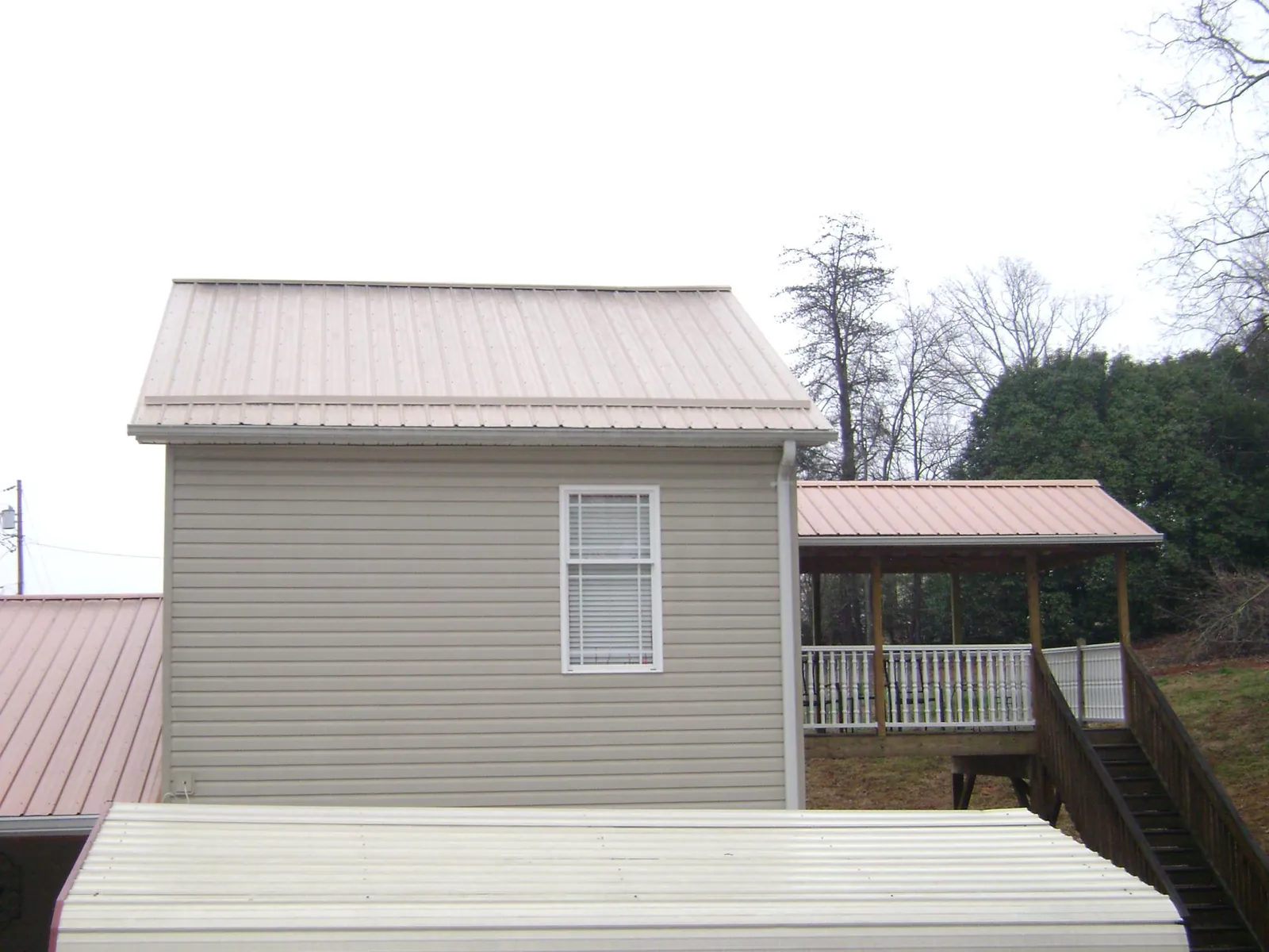 Tan metal roofs on a two story addition and attached porch, from a Roof Replacement job in Trivoli